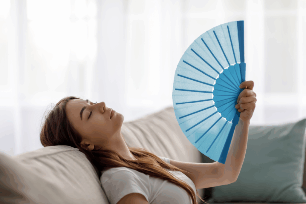 woman leaning back on the couch fanning herself with a blue hand fan because it's hot